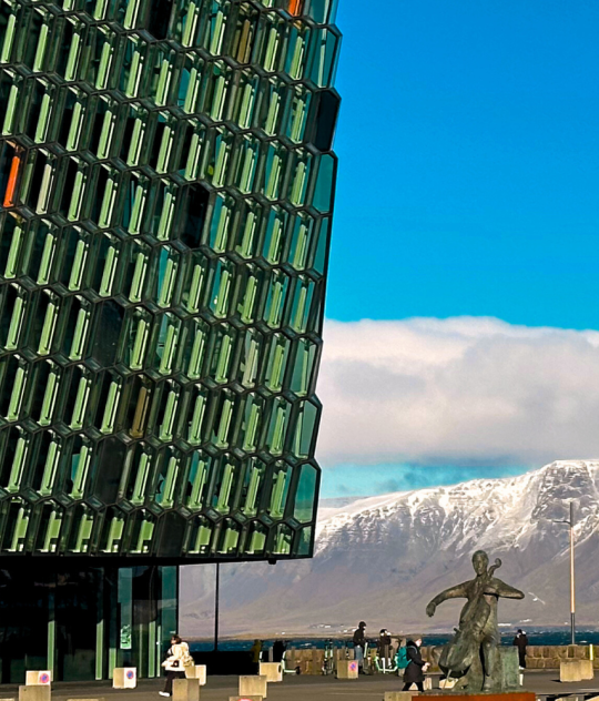 Glass facade of Harpa Concert Hall in Reykjavik with snowy Mount Esja in the background on a bright winter day.