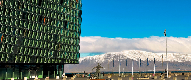 Glass facade of Harpa Concert Hall in Reykjavik with snowy Mount Esja in the background on a bright winter day.