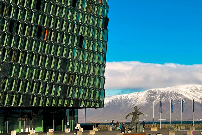 Glass facade of Harpa Concert Hall in Reykjavik with snowy Mount Esja in the background on a bright winter day.