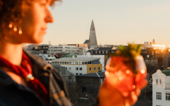 Person enjoying a cocktail overlooking Reykjavík at sunset.