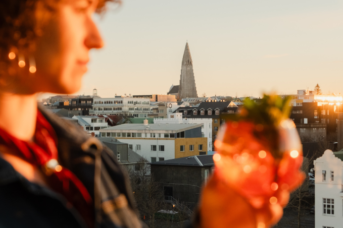 Person enjoying a cocktail overlooking Reykjavík at sunset.