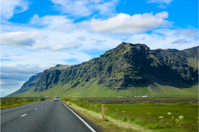 Car driving past dramatic mountains on Iceland's South Coast.