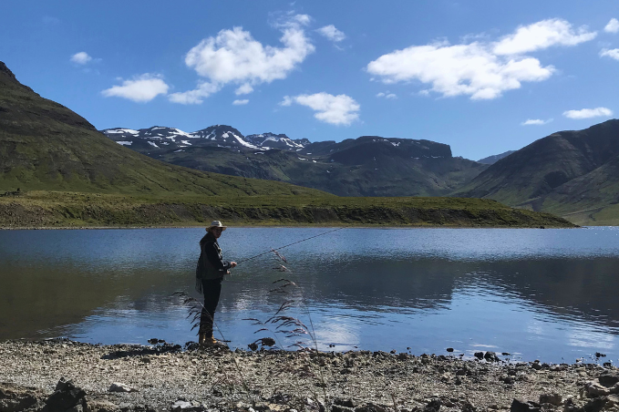 Person fishing in a mountain lake surrounded by Icelandic nature