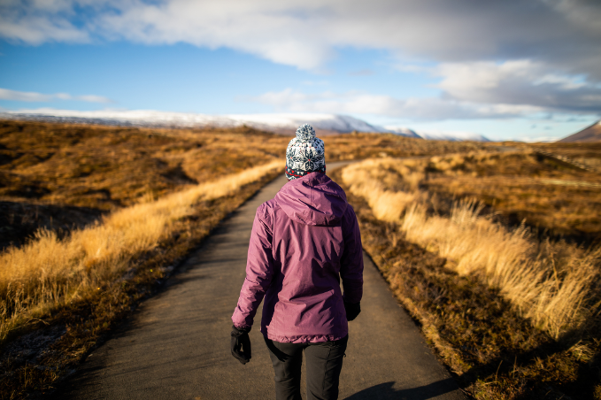 Person wearing a purple jacket, knitted hat and gloves walking through golden autumn grassland.