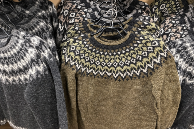 Traditional Icelandic wool sweaters on hangers, with patterned yokes in grey, cream and olive green.
