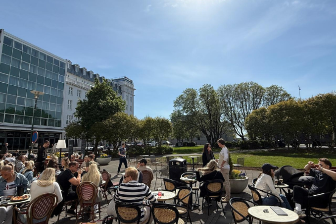 People sitting at an outdoor café in Reykjavík on a sunny day with tables, chairs, and green park surroundings