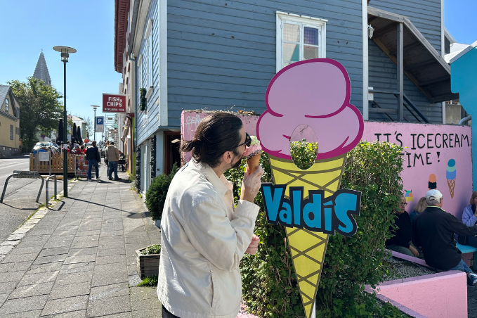 Person eating ice cream next to a Valdís ice cream sign on a sunny street in Reykjavík near the harbour
