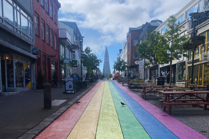 Rainbow-painted Skólavörðustígur street in downtown Reykjavík with shops, cafés and Hallgrímskirkja in the distance.